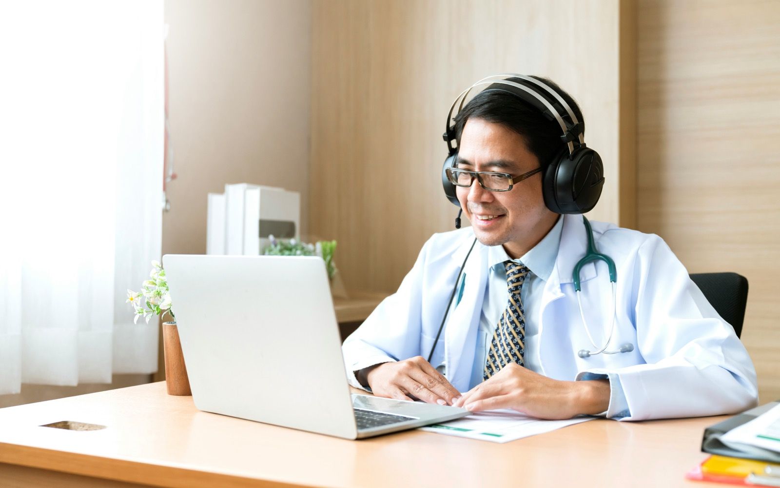 A licensed provider on a telehealth video call, reviewing a patient's case on a laptop